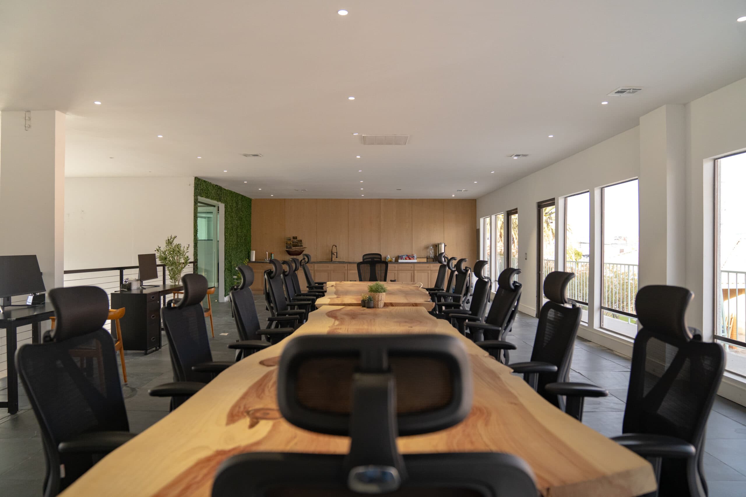 Conference Table 2: long live-edge wood table with black mesh chairs, a wood-paneled kitchenette and a living green wall